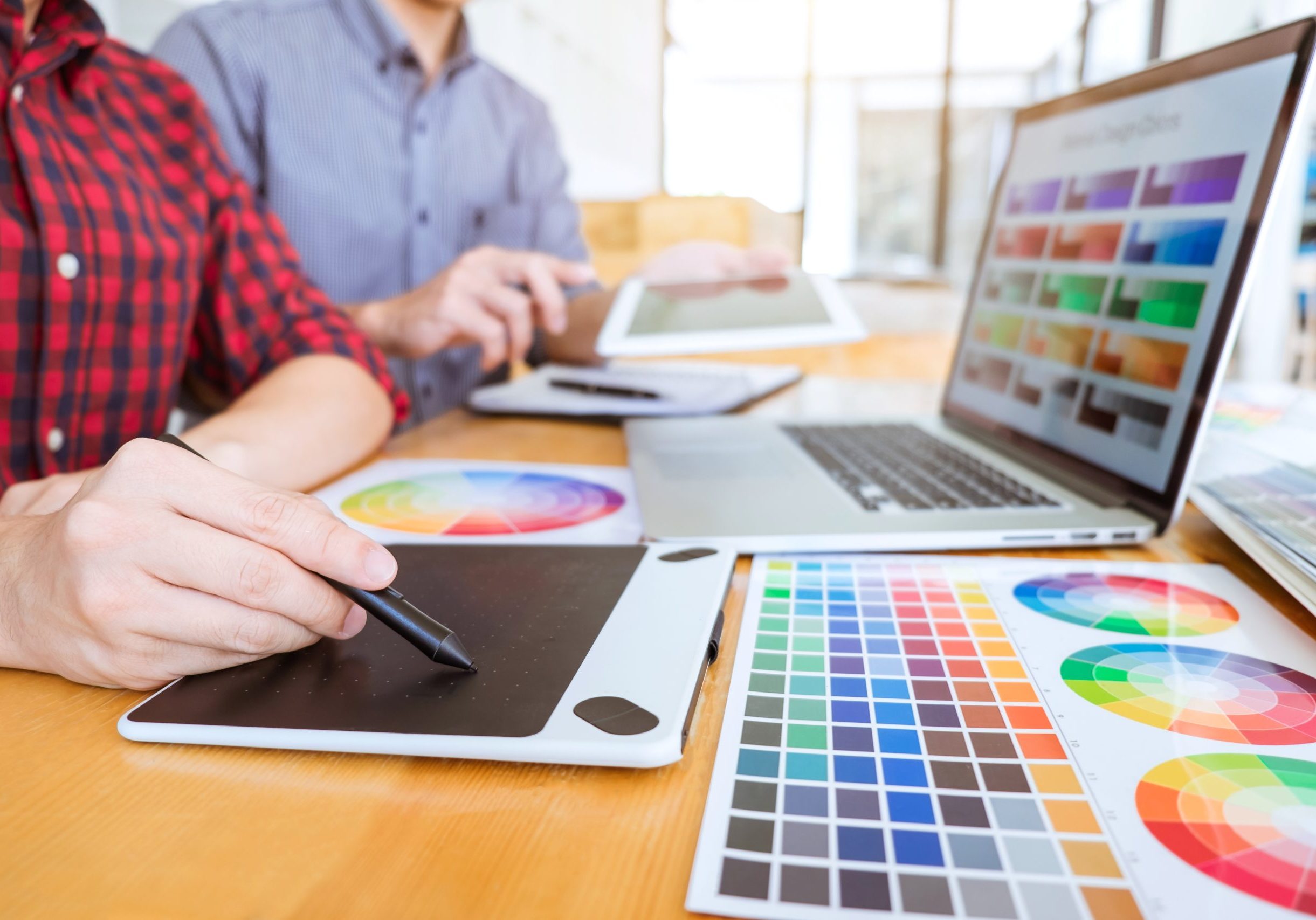 Teamwork of young creative designers working on project together Teamwork of young creative designers working on project together and choose color swatch samples for selection coloring on digital graphic tablet at workspace.
